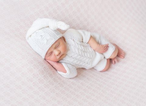Sweet baby sleeping on his side, dressed in knitted white suit and a white hat