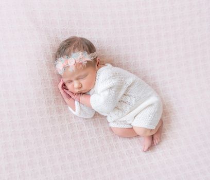 Little kid napping on side, wearing white outfit and a flowery hairband