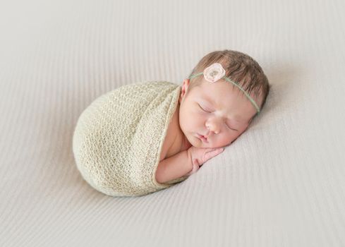 Adorable kid napping wrapped with a scarf, arm hanging out of it, sleeping tight