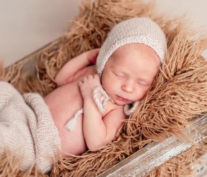 Little cute baby in hat lying covered with light blanket