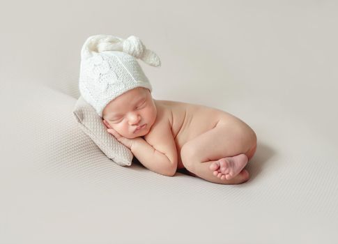 Adorable little baby in knitted hat sleeping on small pillow on cream background