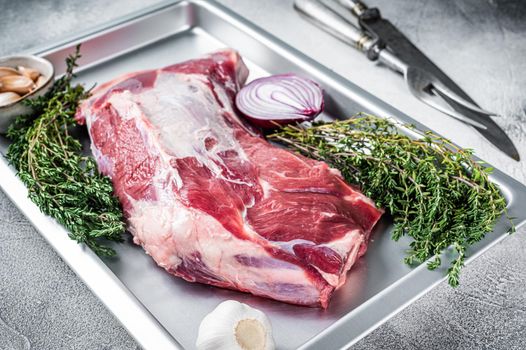 Raw lamb mutton shoulder meat in a baking dish with thyme and garlic. White background. Top view.