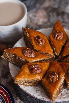 Assorted baklava. A Turkish ramadan arabic sweet dessert on a decorative plate, with coffee cup in the background. Middle eastern food baklava with nuts and honey syrup.