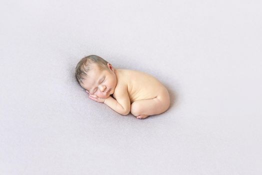 Cute naked baby sleeping on his belly, curled up, laying on white surface