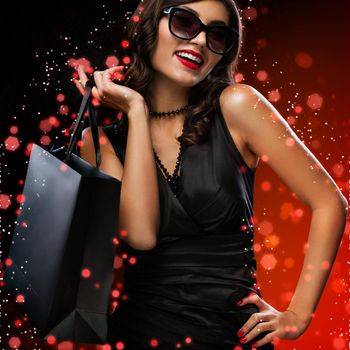 Beautiful young woman make shopping in black friday holiday. Girl with black bag on dark background.