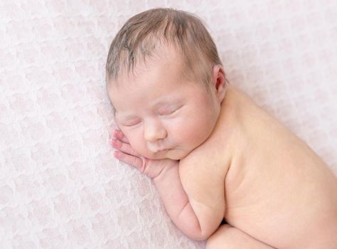 Sweet naked kid sleeping and smiling calmly, hands under his cheek, pastel soft surface, closeup