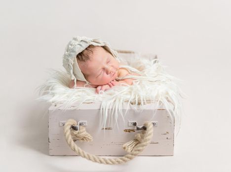 Awesome child sleeping on big white rustic box, wearing a lovely hat, white background