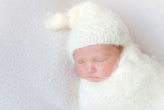 Sweet little infant wearing a warm white hat sleeping, red cheeks, closeup