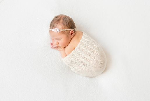 Amazing little baby girl with a headband sleeping tight in a scarf, white surface