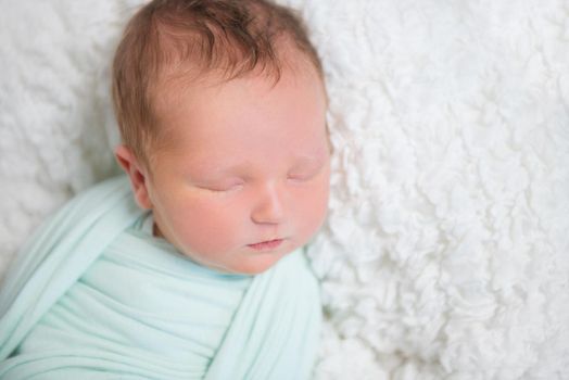 Lovely tiny baby wrapped up in soft light blue blanket resting on soft white surface