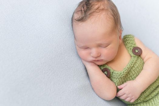 Cute hairy infant wearing summer green knitted costume, sleeping with his hand under the cheek