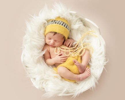 funny sleeping baby in yellow romper with chicken toy on round cot, top, view