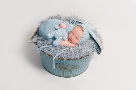 Lovely kid dressed as easter rabbit sleeping with his blue rabbit toy in child's basket