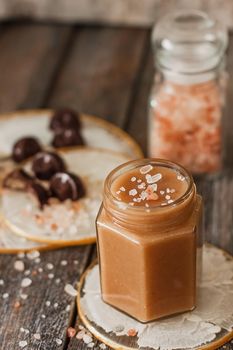 Homemade salted caramel sauce in jar on vintage background.