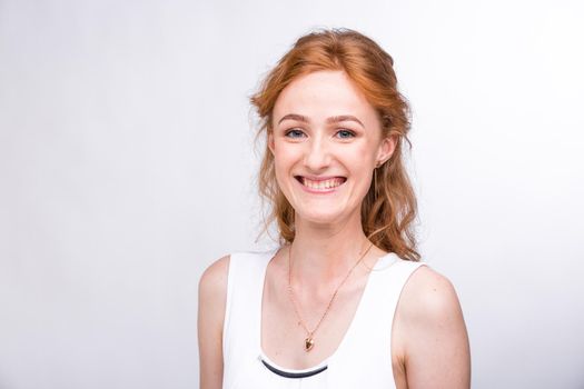 Portrait of a beautiful young female student with a smile in a white shirt of European, Caucasian nationality with long red hair and freckles on her face posing on a white background in the studio.