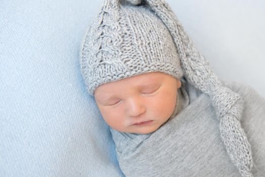 Adorable sweet baby with knitted gray hat on napping wrapped up, curled on his side