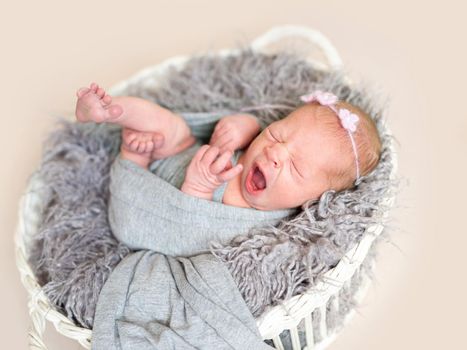 Little cute baby wrapped in gray fabric yawning in bed