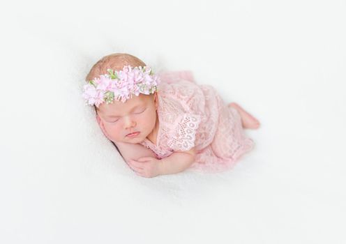 Cute infant with pink flowery hairband dressed in laced costume napping tightly on her side