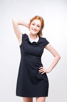 beautiful young girl student, secretary or business lady with charming smile and red curly hair in black dress in white dot and white collar on white gray background in studio.