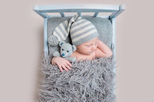 newborn baby sleeping on a bed, in a gray knitted suit with a lovely toy