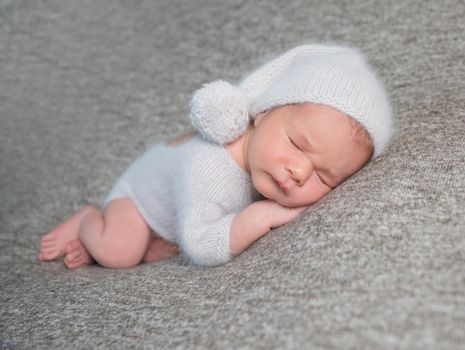 Sweet little baby boy in light blue costume and knitted bonnet with pom pom on grey background.