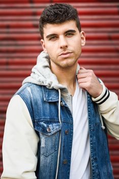 Good looking young man with blue eyes in the street. Model of fashion in urban background wearing white t-shirt, jeans and blue jacket