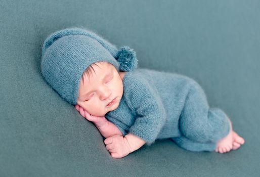 Infant baby boy sleeping in woolen costume with bare feet on blue blanket. Dreamy little child sleeps