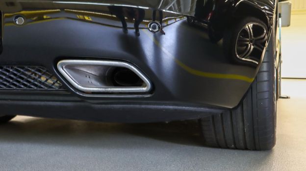 Square tailpipe at the rear right side of a black sports car. Very low plan. The rear bumper, wheel and tailpipe of the packed vehicle are smoke- and gas-free