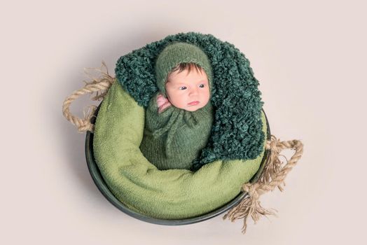 Little newborn baby swaddled in green coccon lying on round basket