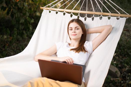 woman outdoors with laptop lies in hammock leisure technology. High quality photo