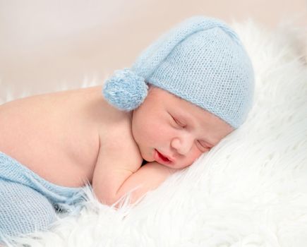 Newborn baby boy sleeping on white wooden crib embracing hare toy. Little boy wearing blue outfit sleeps on small bed