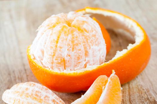 peeled juicy fruit of mandarin with peel lying nearby, closeup
