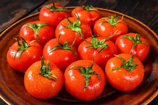 Red ripe tomatoes on rustic plate. Dark Wooden background. Top view.