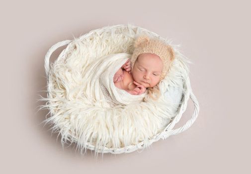 Adorable newborn baby napping in white round basket, top view. Little newborn baby in funny bonnet with ears