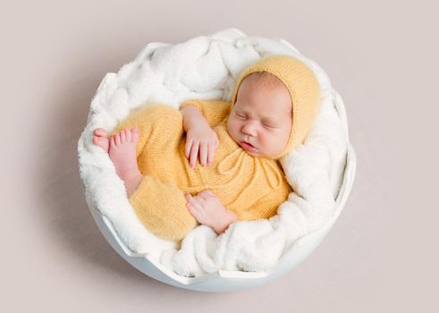 Sleeping newborn baby boy curled up on round basket, top view