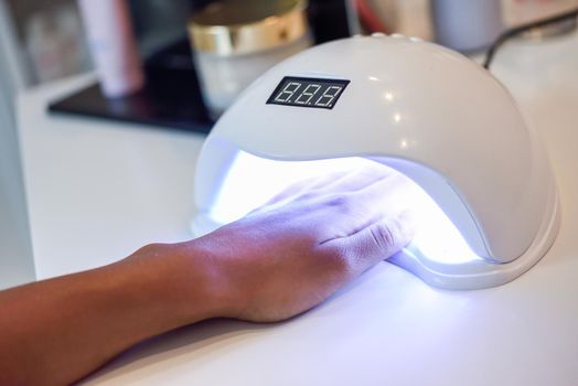 Manicured nails in UV lamp. Small nail art and manicure business. Hands of woman in a wellnes salon