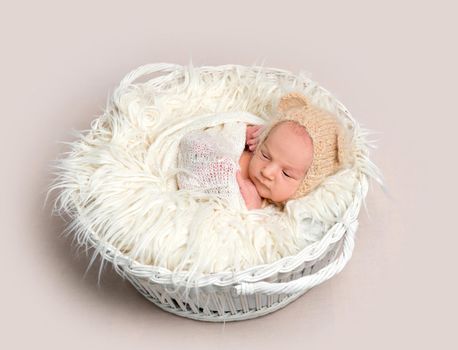 Adorable newborn baby napping in white round basket, top view. Little newborn baby in funny bonnet with ears