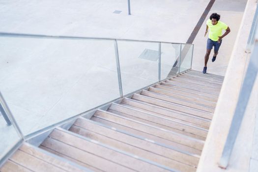 Black man running upstairs outdoors. Young male exercising in urban background.