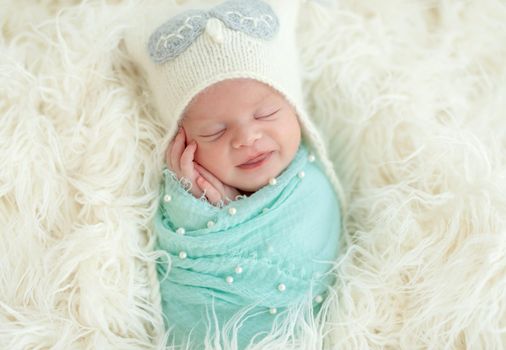 Cute smiling newborn baby boy sleeping on a wool blanket in knitted hat