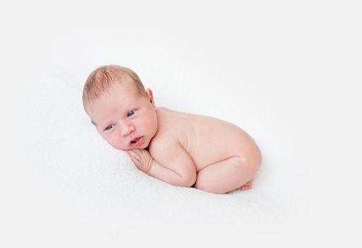 Little newborn boy with clear blue eyes and open mouth lying on his tummy on the bed