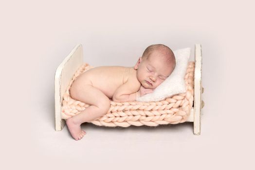 Infant baby lying on a small crib with one leg on the floor. Newborn baby resting on the bed