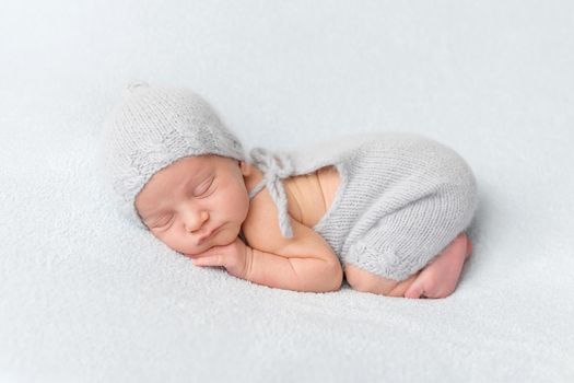 Tender little baby comfortably sleeping on belly. Newborn in tushy up pose on white blanket