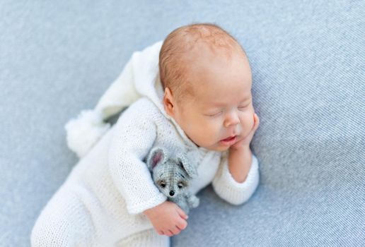 Nice newborn drowsing holding toy on gray blanket