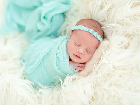 Sleeping adorable newborn baby child, in blue colored blanket and with floral headband