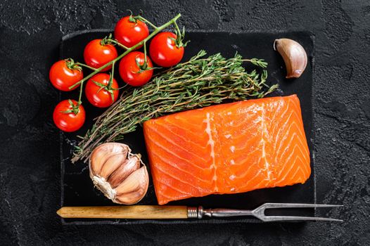 Protein vegetarian diet - raw salmon fillet steak with herbs and tomato. Black background. Top view.