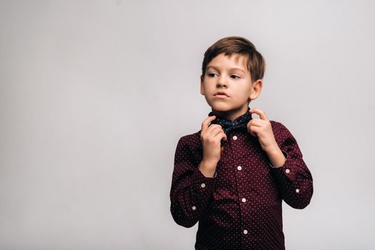 A beautiful boy in a shirt and bow tie stands on a gray background.