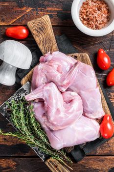 Raw hare legs on a butcher board with thyme. Dark wooden background. Top view.