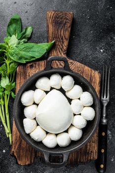 Mozzarella cheese mini balls in pan with basil. Black background. Top view.