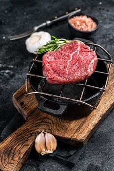 Raw fillet mignon beef steak on a grill with herbs. Black background. Top view.