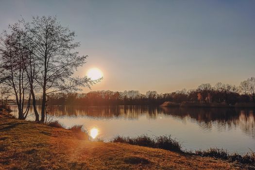 Vivid autumn sunset. Autumn landscape of sunset over river with shining grass on shore. Scenic nature at bright evening with colorful sky.